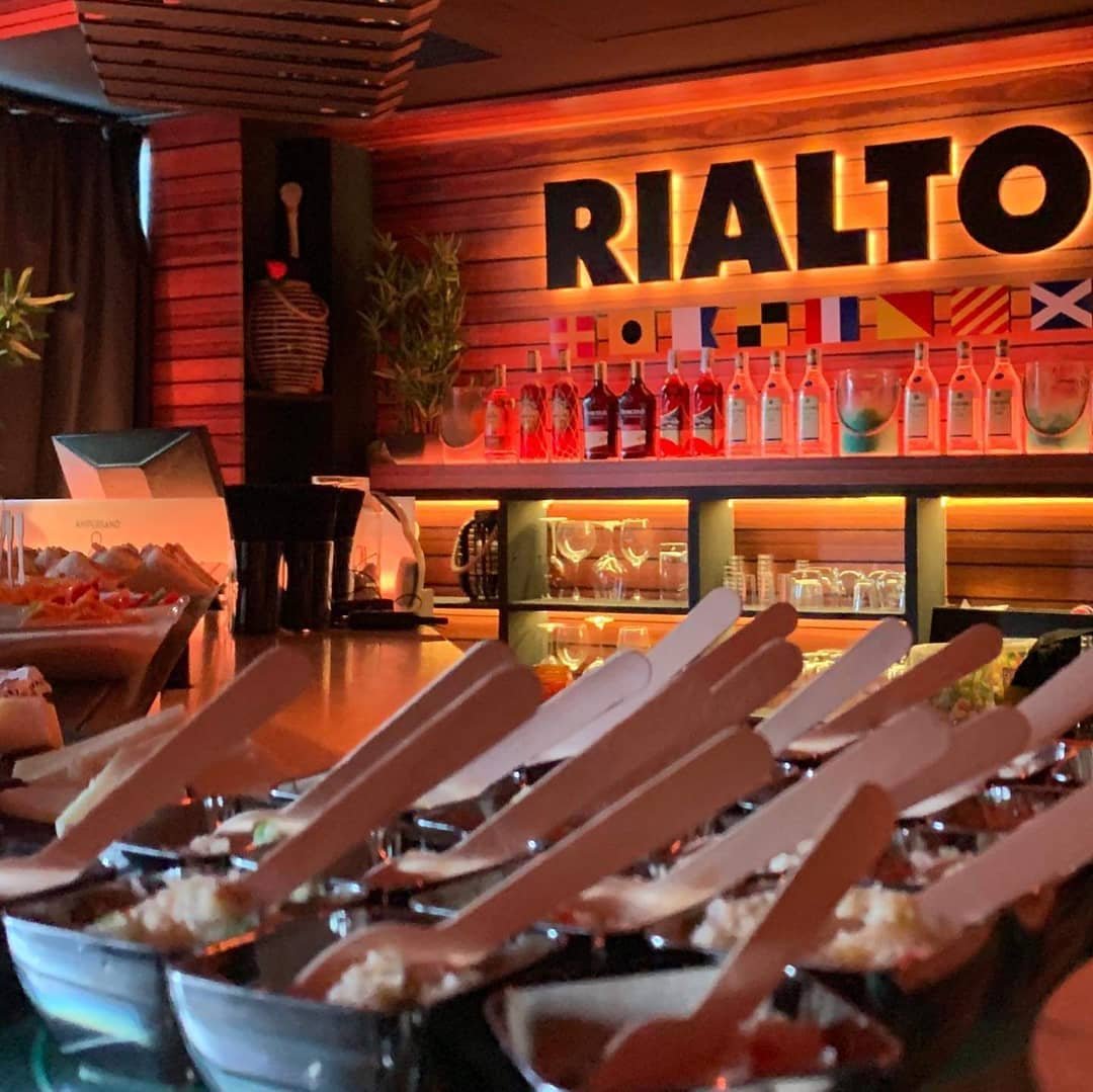 Vasitos de picoteo en la barra bajo el letrero luminoso de Rialto con las banderas náuticas